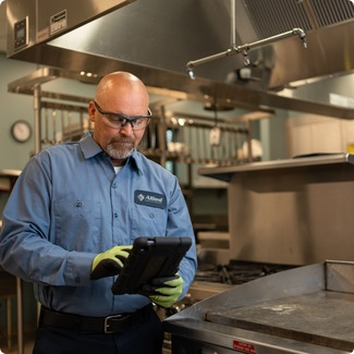 Allied Service Group technician reviewing a tablet beside cooking equipment in a commercial kitchen