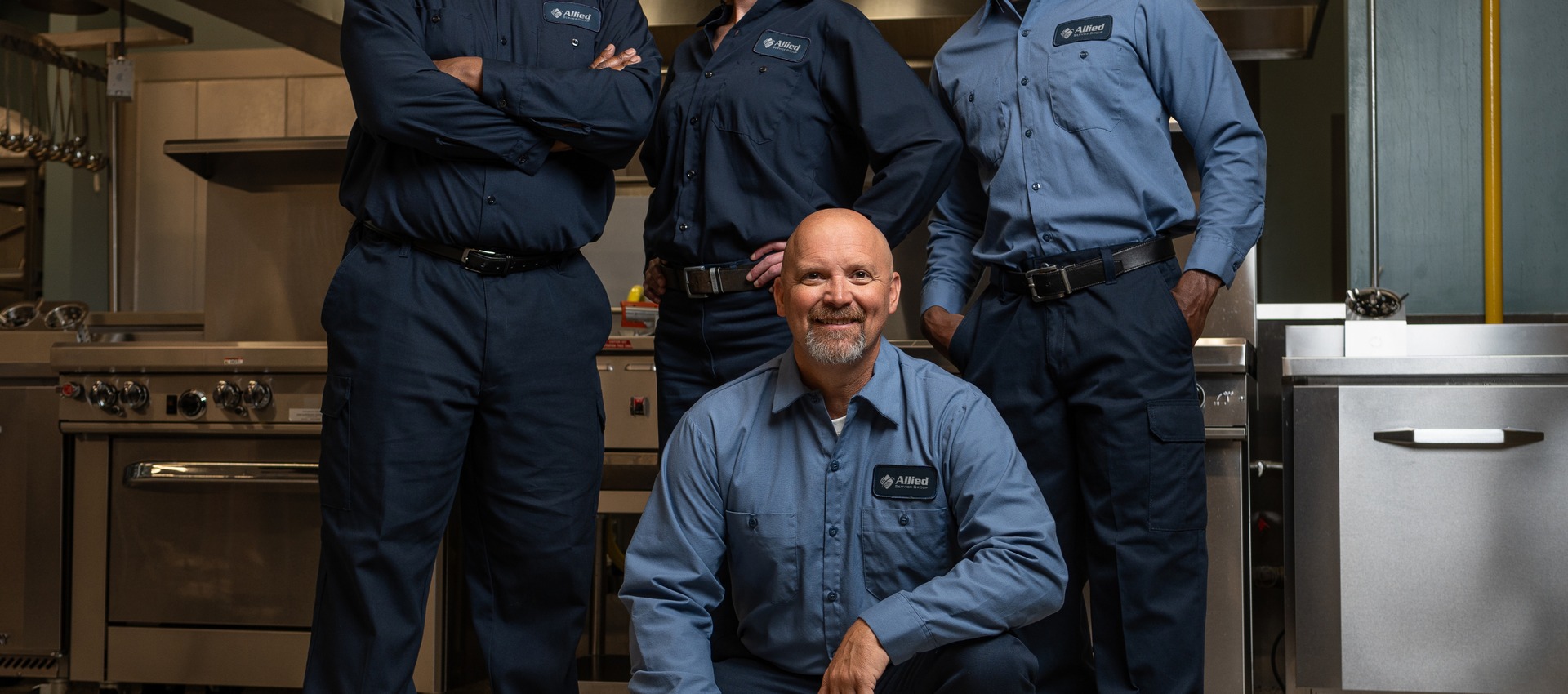 Four Allied Service Group technicians posing together in a commercial kitchen