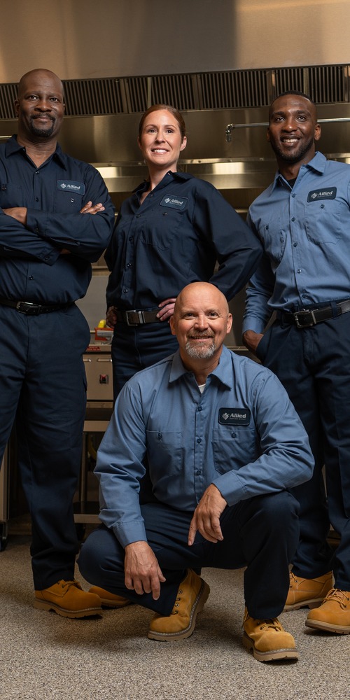 Four Allied Service Group technicians posing together in a commercial kitchen