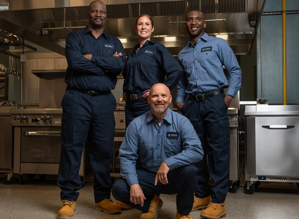 Four Allied Service Group technicians posing together in a commercial kitchen