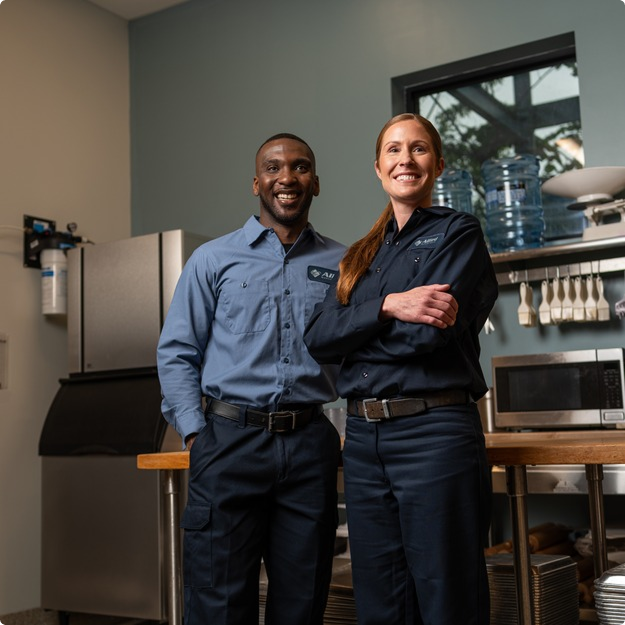 Two Allied Service Group technicians standing side by side with arms crossed in a commercial kitchen