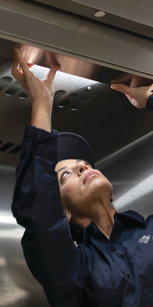 Allied Service Group technician reaching up to inspect stainless steel commercial kitchen equipment