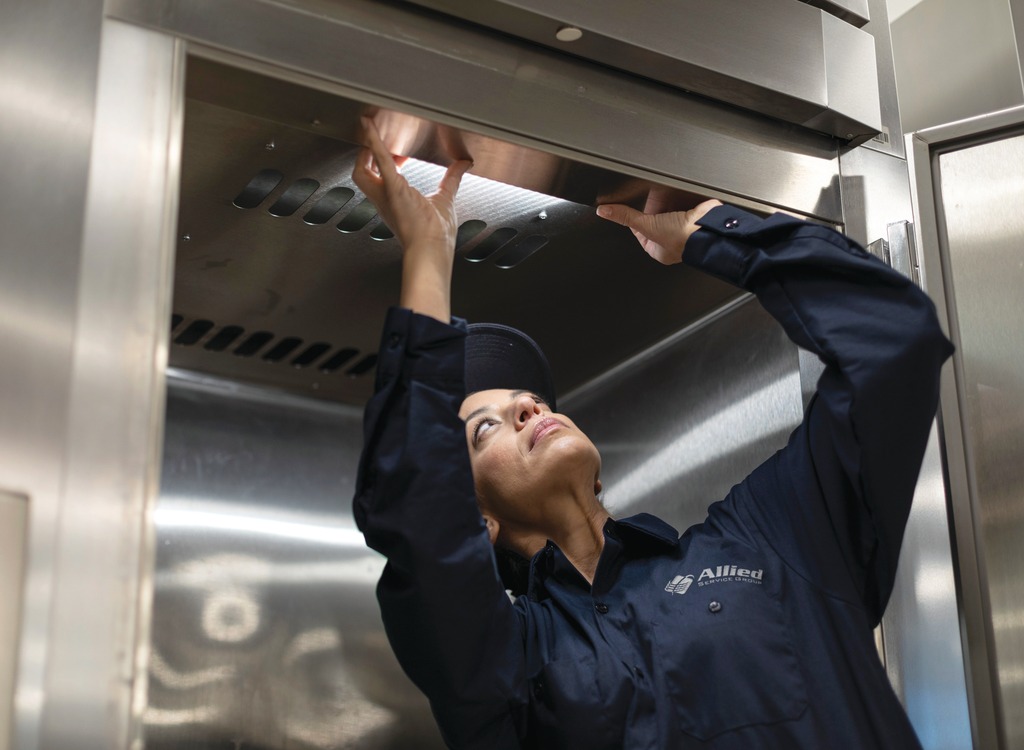 Allied Service Group technician reaching up to inspect stainless steel commercial kitchen equipment
