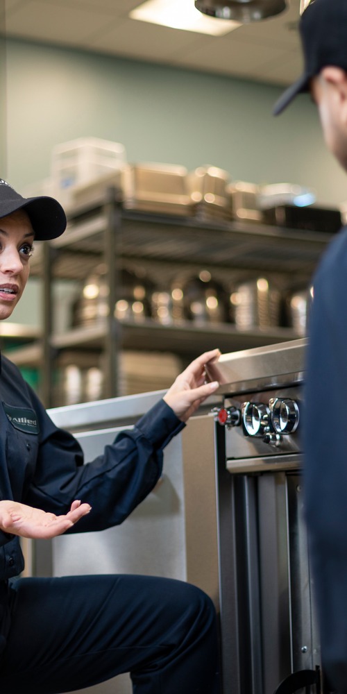 Two Allied Service Group technicians talking beside equipment in a commercial kitchen