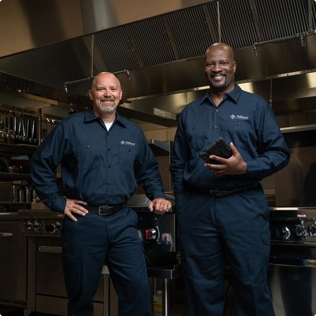 Two Allied Service Group technicians standing in a commercial kitchen, one holding a tablet