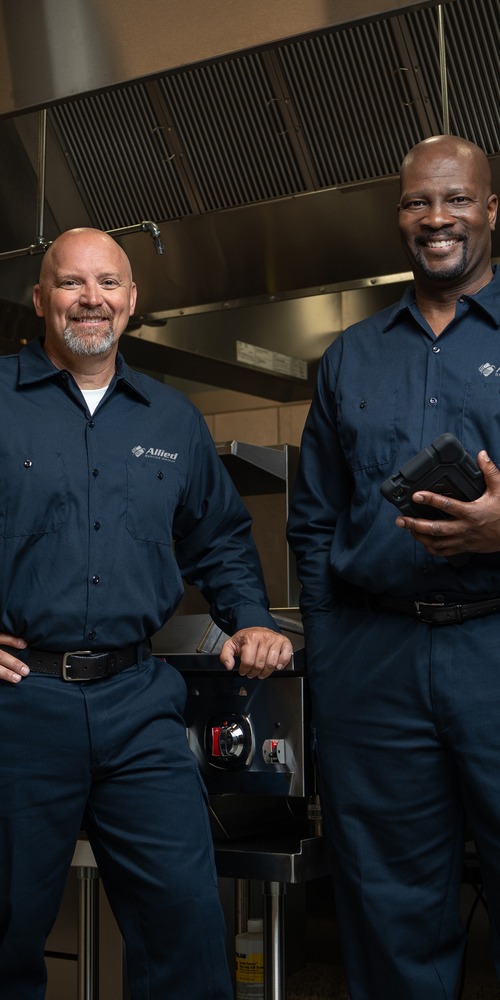 Two Allied Service Group technicians standing in a commercial kitchen, one holding a tablet