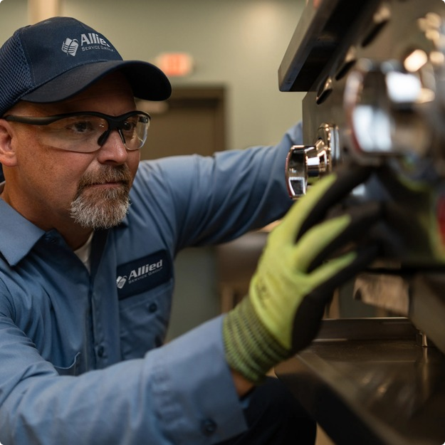 Allied Service Group technician in safety glasses and work gloves servicing commercial kitchen equipment