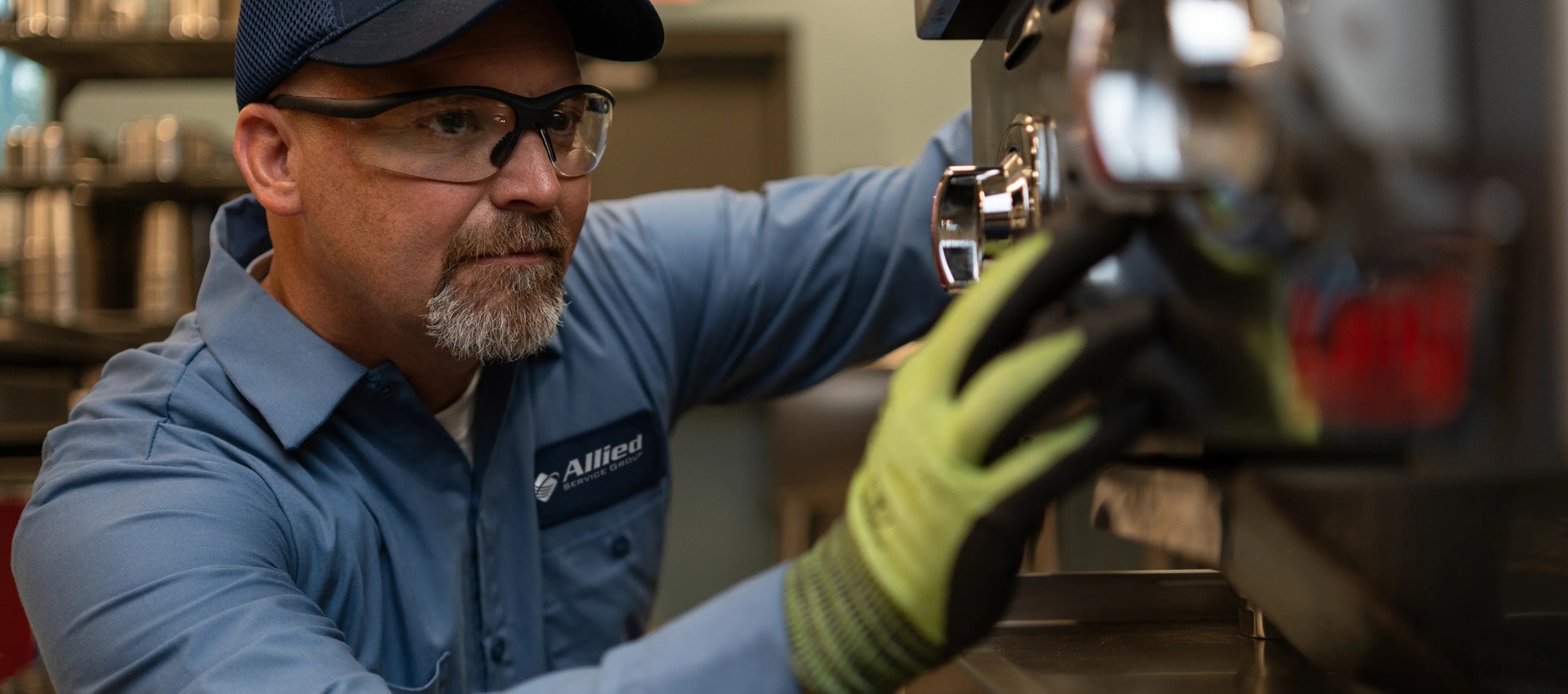 Allied Service Group technician in safety glasses and work gloves servicing commercial kitchen equipment