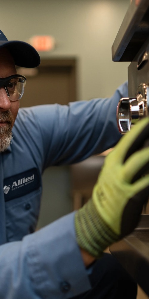 Allied Service Group technician in safety glasses and work gloves servicing commercial kitchen equipment