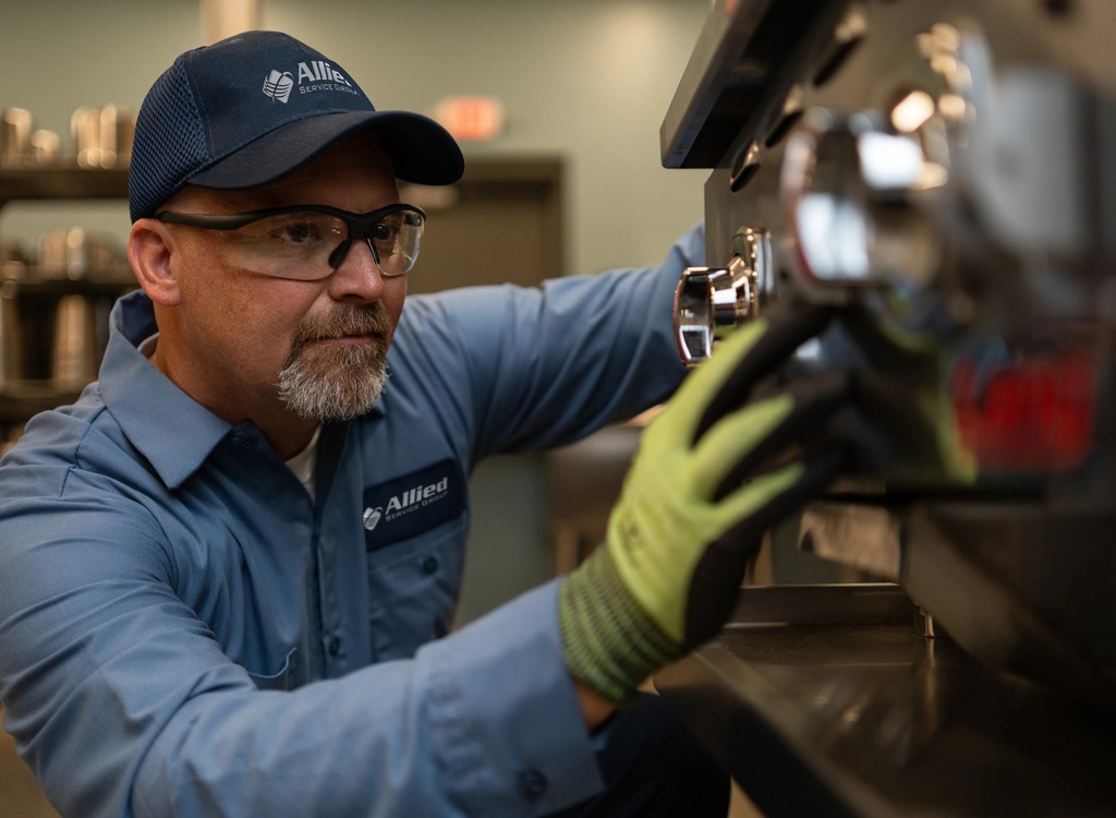 Allied Service Group technician in safety glasses and work gloves servicing commercial kitchen equipment