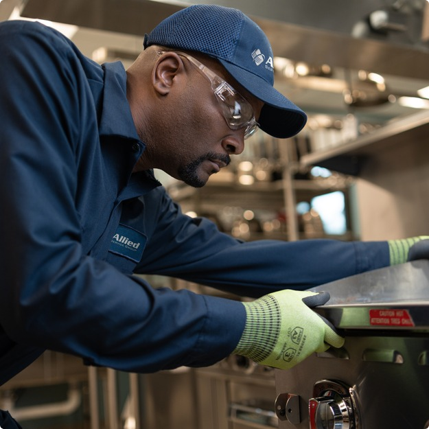 Allied Service Group technician in safety glasses and gloves working on a commercial cooking appliance