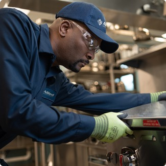 Allied Service Group technician in safety glasses and gloves working on a commercial cooking appliance