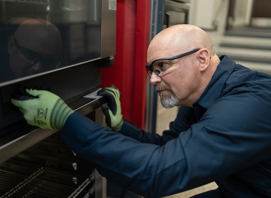Service technician in safety glasses inspecting the door of a commercial oven