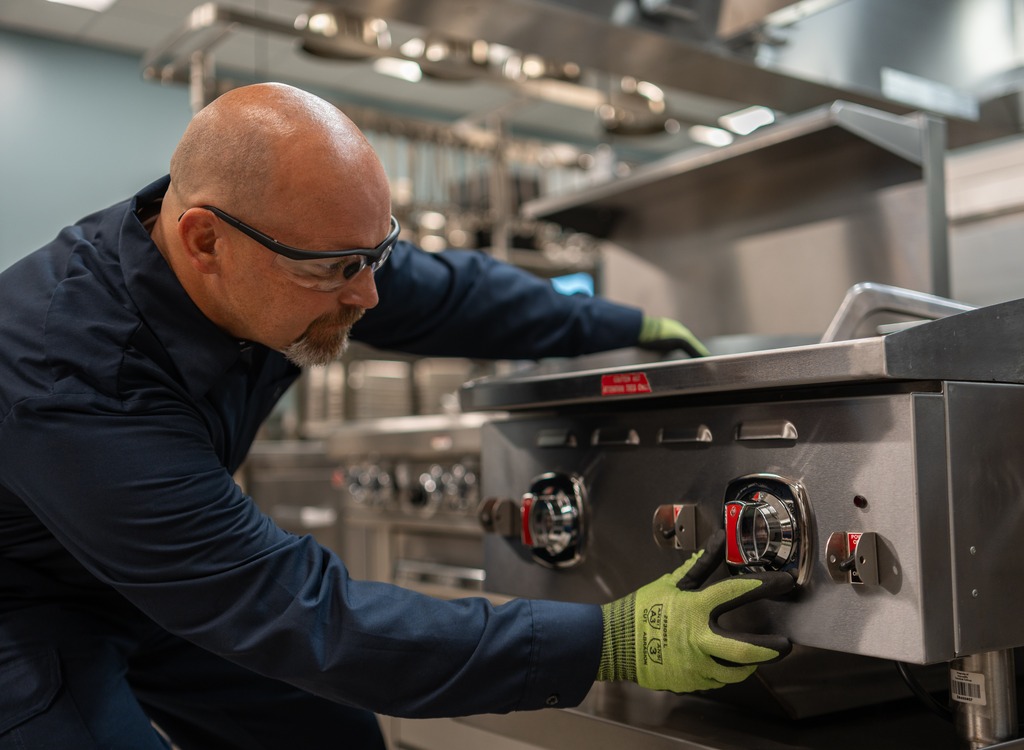 Allied Service Group technician adjusting the control knobs on a commercial range